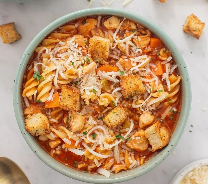A bowl of Chicken Parm Soup garnished with cheese and herbs