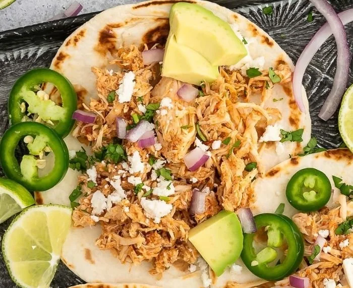 Delicious crockpot shredded chicken tacos served on a plate with toppings.