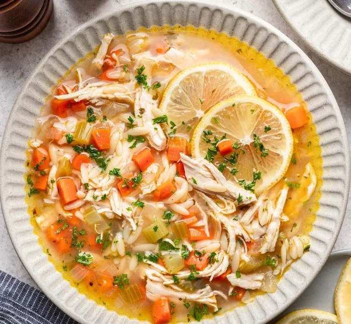 Bowl of Lemon Chicken Orzo Soup with fresh herbs and lemon slices