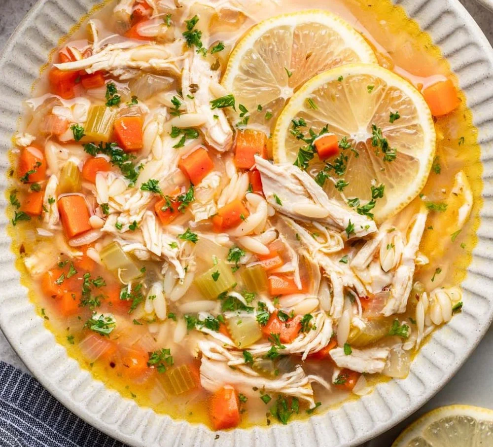 Bowl of lemon chicken soup garnished with fresh herbs and lemon slices