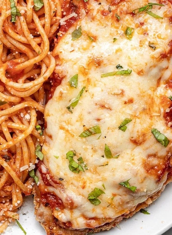 Easy baked chicken parmesan dish served with pasta and fresh herbs